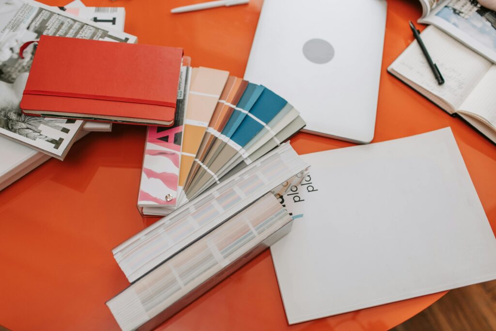 A vibrant workspace featuring design swatches, books, and a laptop on a bright orange desk.
